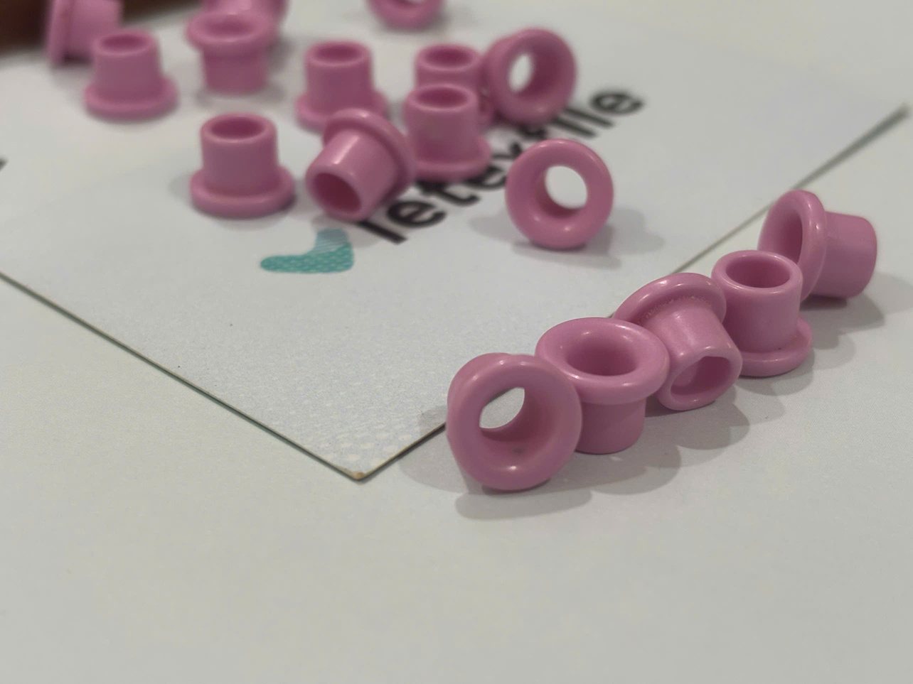Ceramic Eyelet Risks: 7 Preventive Checks 2 A close-up view of numerous pale pink, tubular ceramic guides distributed randomly across a white surface printed with the faint text "vietextile".