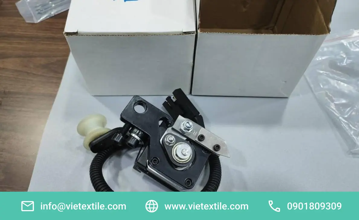 Cận cảnh bộ phận cơ khí dệt may gồm Motor bước BE309505, puli và dây cáp, đặt trên nền trắng cạnh hộp.